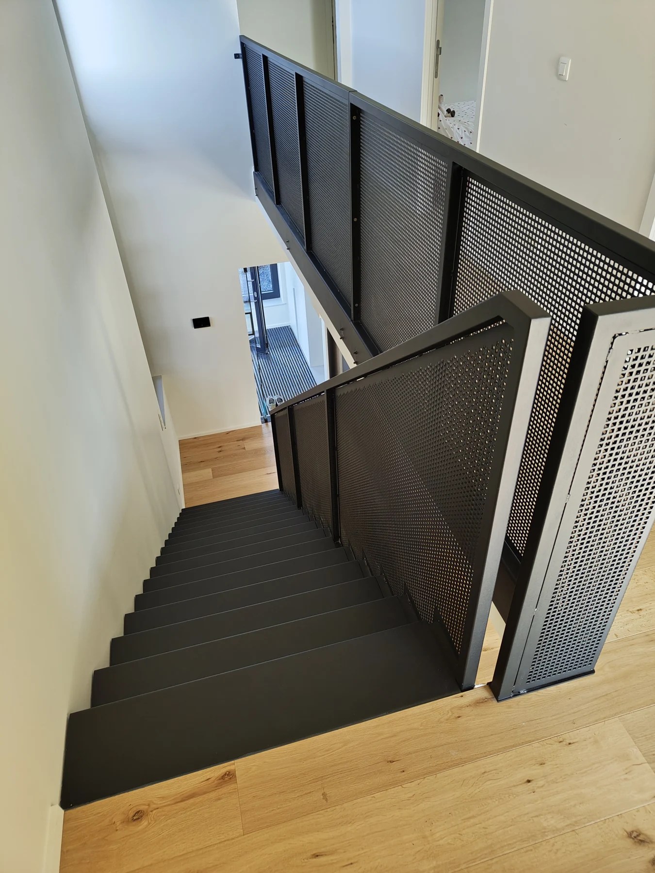 Escalier noir et garde-corps perforé, vus depuis le palier